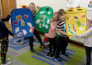 Dzieci prezentują kosze z naklejonymi emblematami śmieci.